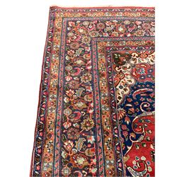 Persian Meshed crimson ground carpet, centre floral design medallion within a field of trailing branches and flower heads, scrolled spandrels decorated with flower heads, the main border decorated with stylised plant motifs within guard rails 