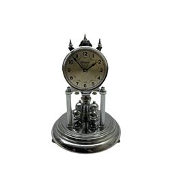 A 20th century German “Olympia” torsion suspension clock, with a silver effect base and four ball rotary pendulum, silver effect dial with Arabic numerals and minute track, with steel baton hands, plain silvered bezel under an acrylic dome.
No Key. 

