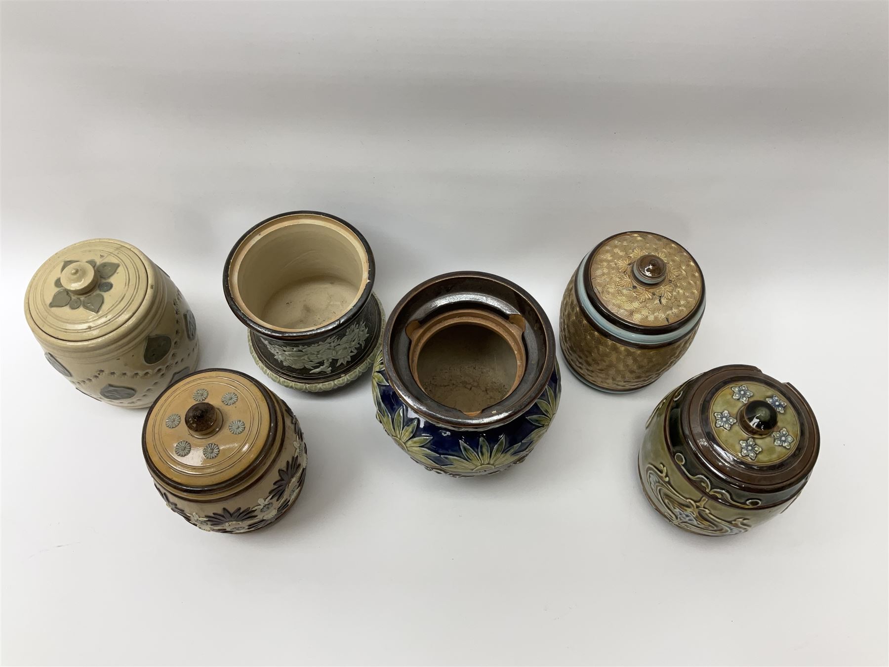 A group of Doulton Lambeth and Royal Doulton tobacco jars, to include examples with relief moulded foliate decoration, each with impressed marks and markers monograms beneath. 