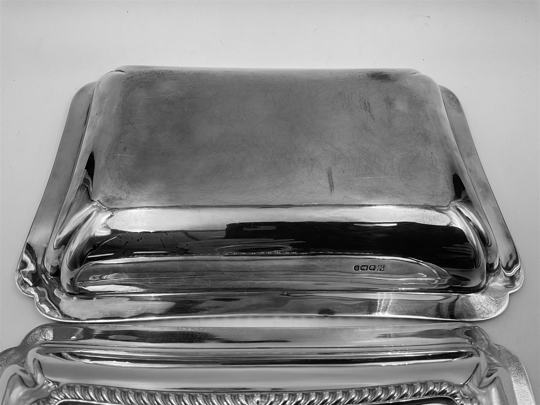 Early 20th century silver entree dish and cover, of rectangular form with shaped corners and oblique gadrooned borders to base and cover, the cover with loop 'bamboo' handle, hallmarked Thomas Bradbury & Sons Ltd, Sheffield 1930, including handle H10.5cm L24.5cm