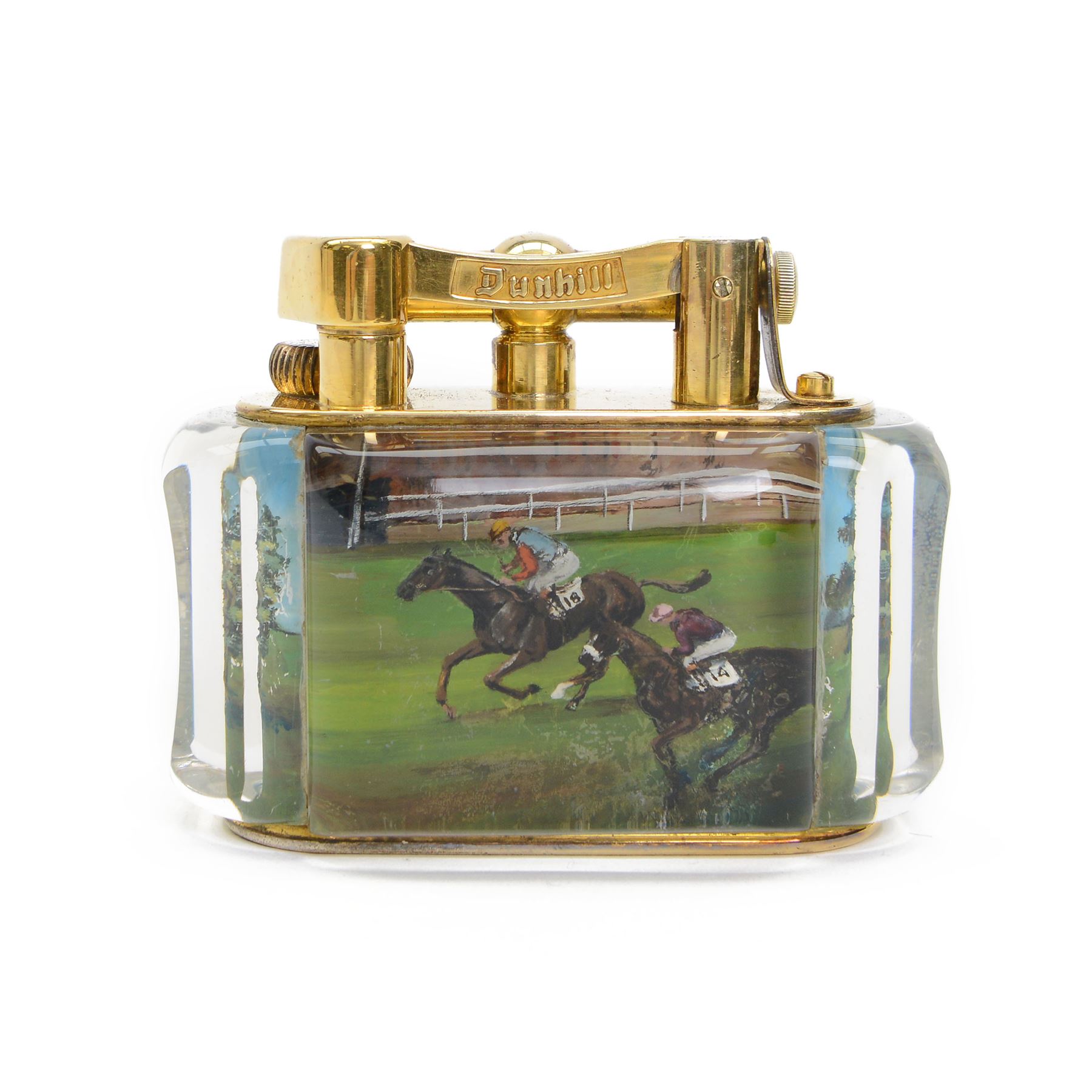 Rare one off special commission Dunhill Sporting Horse Racing half-giant 'Aquarium' table lighter, circa 1955, the lucite panelled body engraved in reverse intaglio technique and hand-painted with Nicholas Nickleby in action, winner of the Royal Hunt Cup, Ascot June 1955, the reverse with jockey Willie Snaith mounted upon Nicholas Nickleby, the gold plated top with arm stamped Dunhill Reg. No 737418, the base stamped DUNHILL LIGHTER, H7.5cm W10cm D5cm

Provenance:
Commissioned by the owner of Nicholas Nickleby, the lighter was gifted to Colin Hetherton, a young veterinary surgeon whose intervention saved Nickleby from certain retirement. Hetherton’s expert care and persistence brought the horse back to full health, culminating in a win that stunned the Ascot crowd.