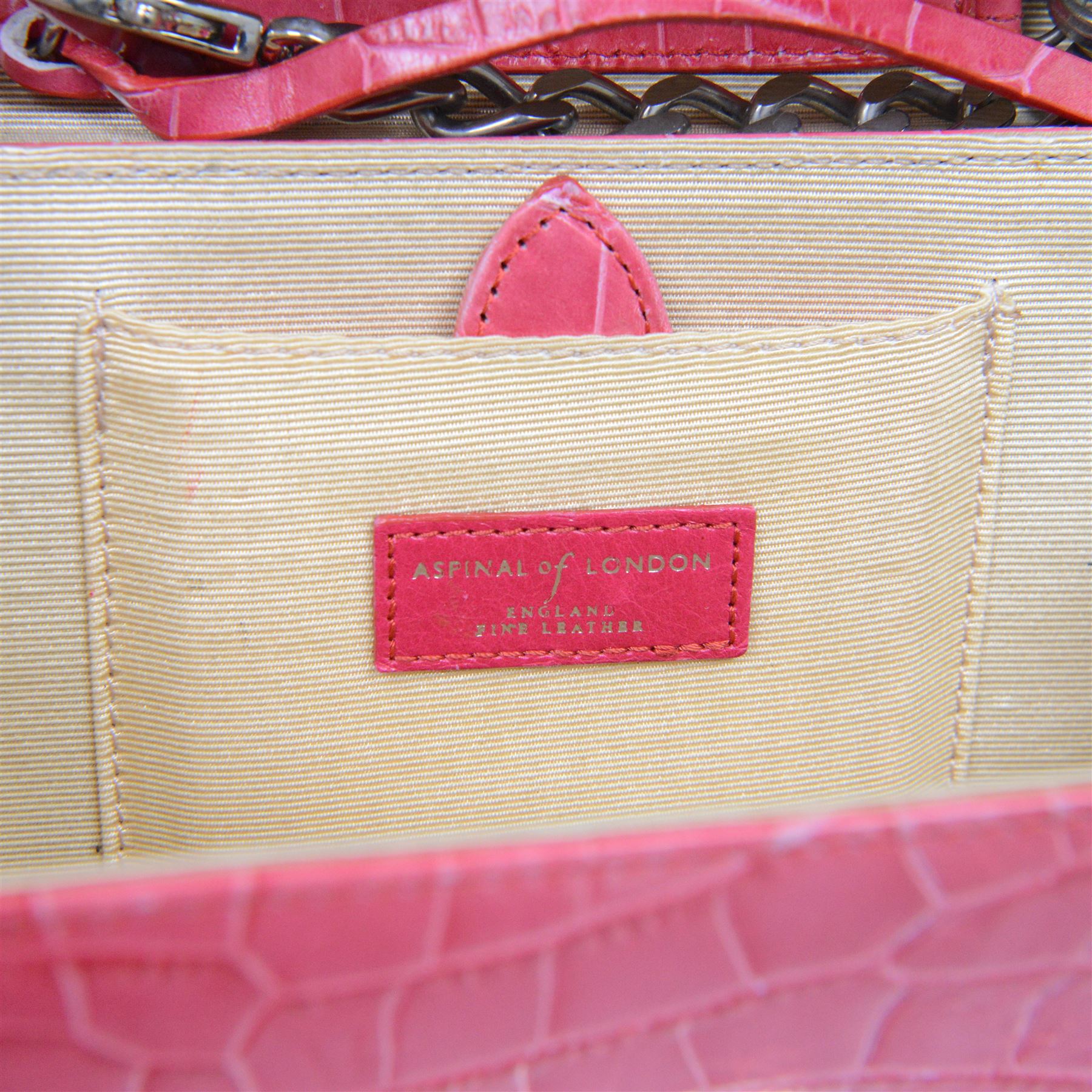 Aspinal of London fuchsia pink crocodile-embossed leather clutch bag with silver-tone shield-shaped clasp engraved Aspinal of London, the flap opening to a beige fabric-lined interior fitted with a zip pocket, slip pocket, integrated mirror and detachable chain shoulder strap, leather brand label stamped Aspinal of London England Fine Leather, accompanied by an Aspinal of London dust bag, W23cm H17cm