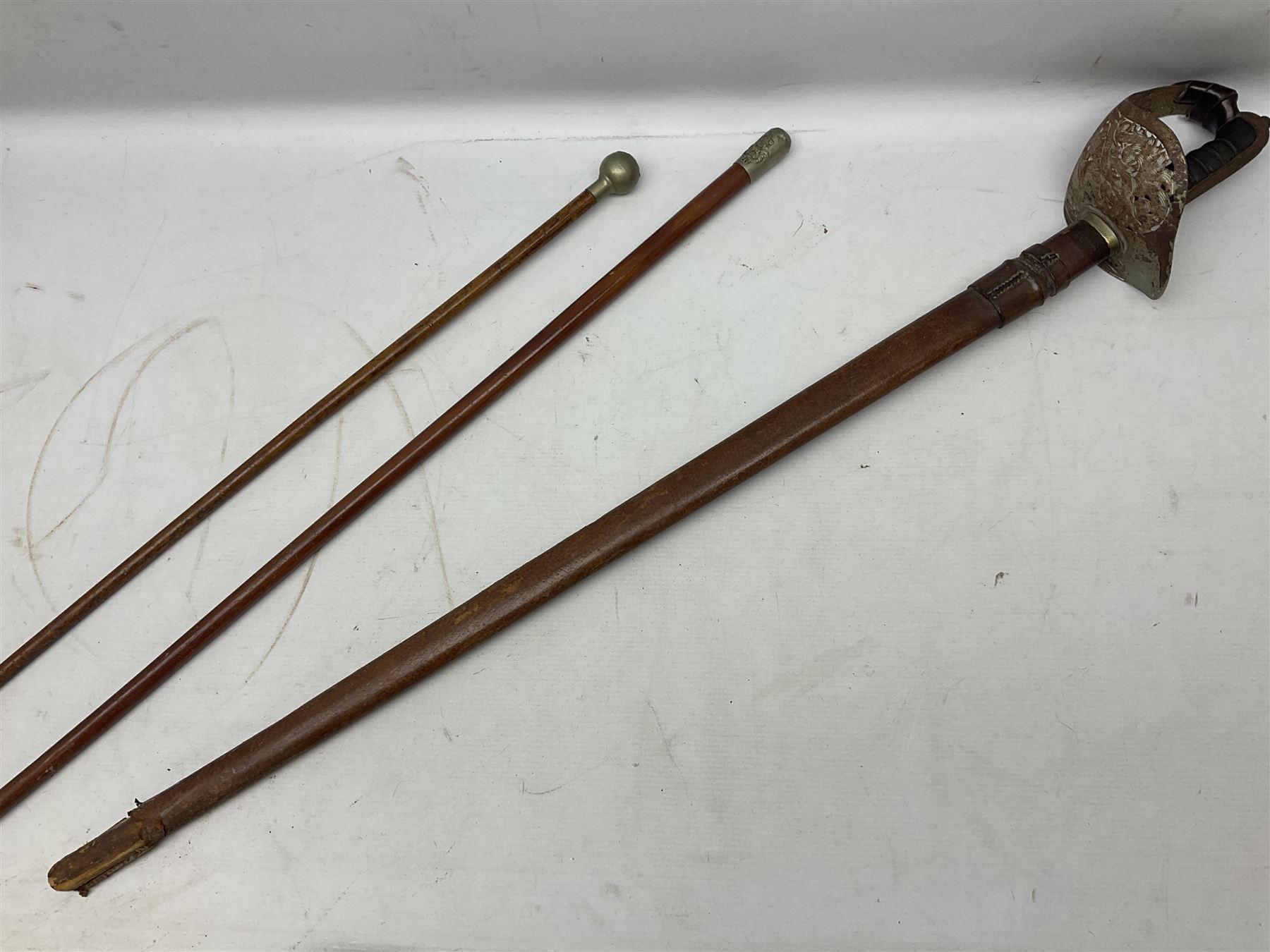 George V 1897 pattern Army Officer's sword by Henry Wilkinson Pall Mall London, the 82.5cm 'London Made' blade etched to both sides with Royal Crests and cyphers etc, pierced half-basket hilt with wire-bound fish skin grip and remains of leather knot strap; in leather covered field service scabbard L101cm overall; and two 14th Prince of Wales Own swagger sticks (3)