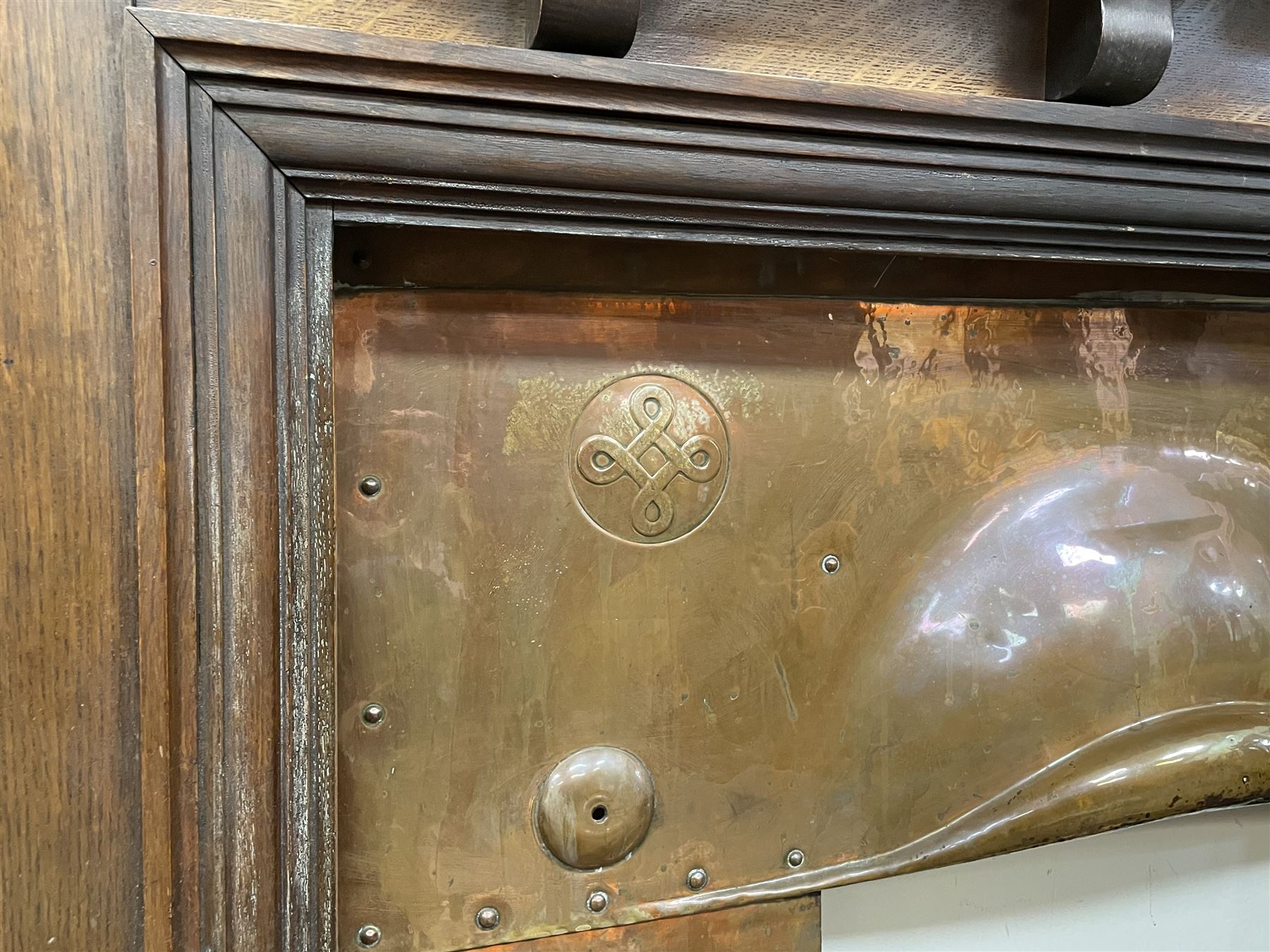 Late 19th/early 20th century fireplace, oak surround with projecting dentil cornice over bevelled mirror and shelf, with copper inset decorated with Heraldic knot motifs and rivets, together with various fire accessories 
