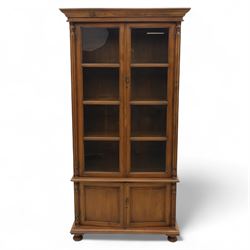 Pair of late 20th century Thai hardwood display cabinets, each with moulded cornice over twin glazed doors enclosing adjustable shelves, panelled cupboard doors below flanked by fluted columns, raised on bun feet