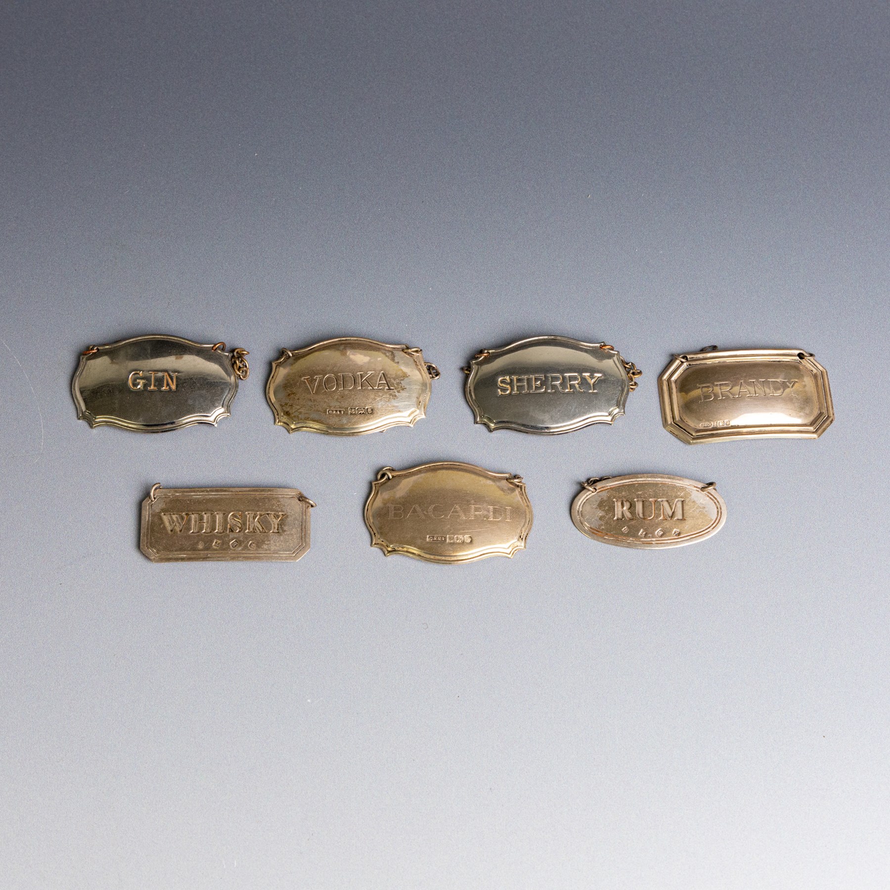 Five silver decanter labels, of varying design, including Bacardi, Vodka, Rum, Brandy and Whisky, all hallmarked together with two silver plated Gin and Sherry examples