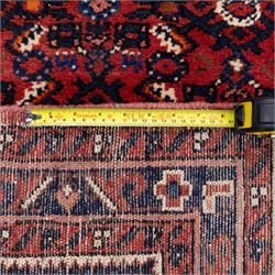 North West Persian Malayer hand-knotted runner, decorated with a dense all-over pattern of small repeating boteh and rosette motifs on a rich madder red ground, field filled with geometric floral elements arranged in a lattice design, framed by a narrow main border and flanked by slender guard borders, with cotton fringe ends 