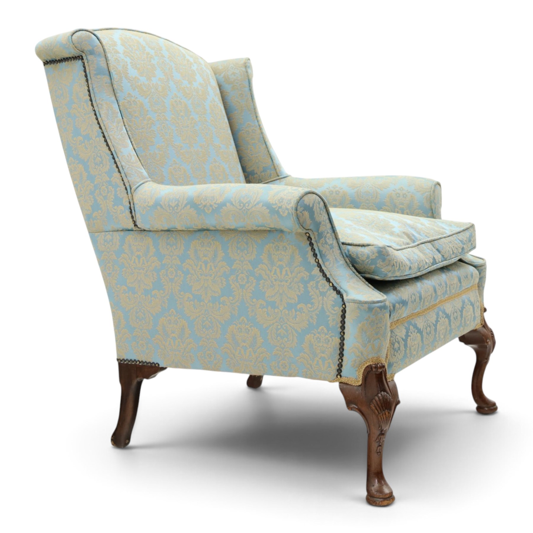 Georgian design carved mahogany framed wingback armchair, high wingback over sprung seat and loose cushion with rolled arms, upholstered in cyan ground gilt foliate damask fabric, on shell-carved cabriole supports with pad feet