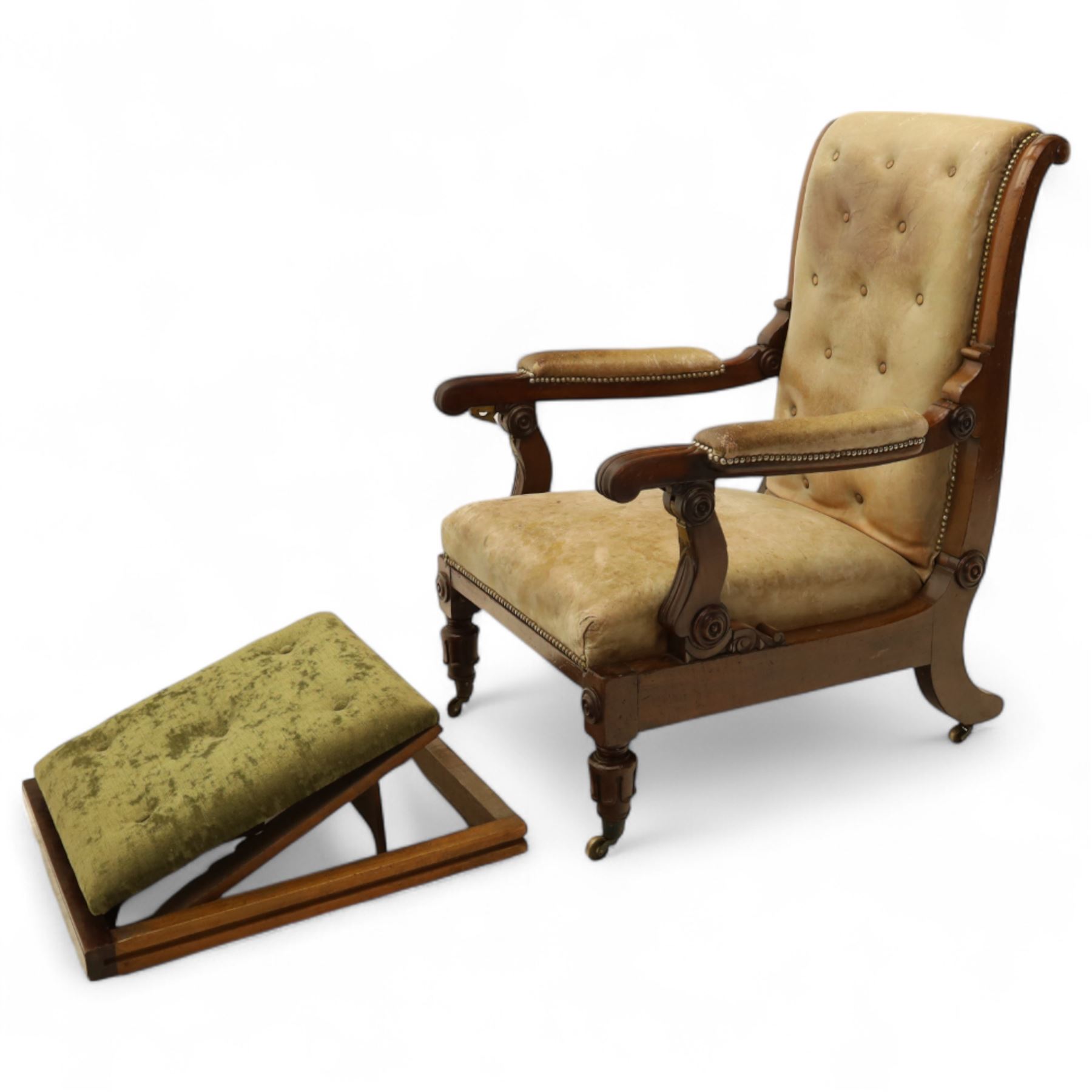 William IV mahogany gentleman's library reclining armchair, leather button upholstered and brass-studded back and seat, above leather-covered arms terminating with carved roundels and foliate scroll-carved ends, underside with brass mechanical trigger reclining lever, the apron with retractable foot rest, supported on lappet carved and turned legs with brass castors, circa 1835