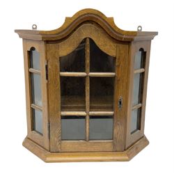 Glazed oak wall cabinet with arched top and projecting cornice, the hinged panelled door opening to reveal shelved interior, with ornate coppered escutcheon, H57cm W56cm D19cm