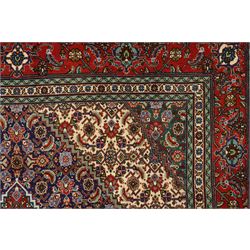 North West Persian Tabriz hand-knotted rug, ivory field with a central lozenge shaped medallion in indigo and madder red, issuing an ornamented arrangement of Herati style motifs, rosettes and angular floral elements, conforming spandrels on an ivory ground, main border in madder red with stylized vinery and palmettes, flanked by multiple guard border, with cotton fringe ends 