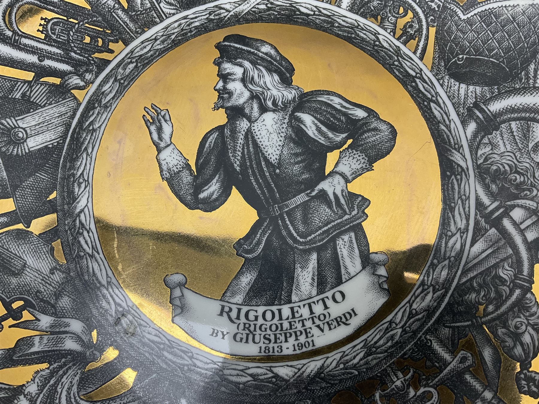 Three Fornasetti plates from the Melodramma series, each depicting a operatic portraits within a border of operatic emblems on gilt ground, with printed mark beneath, D25cm 