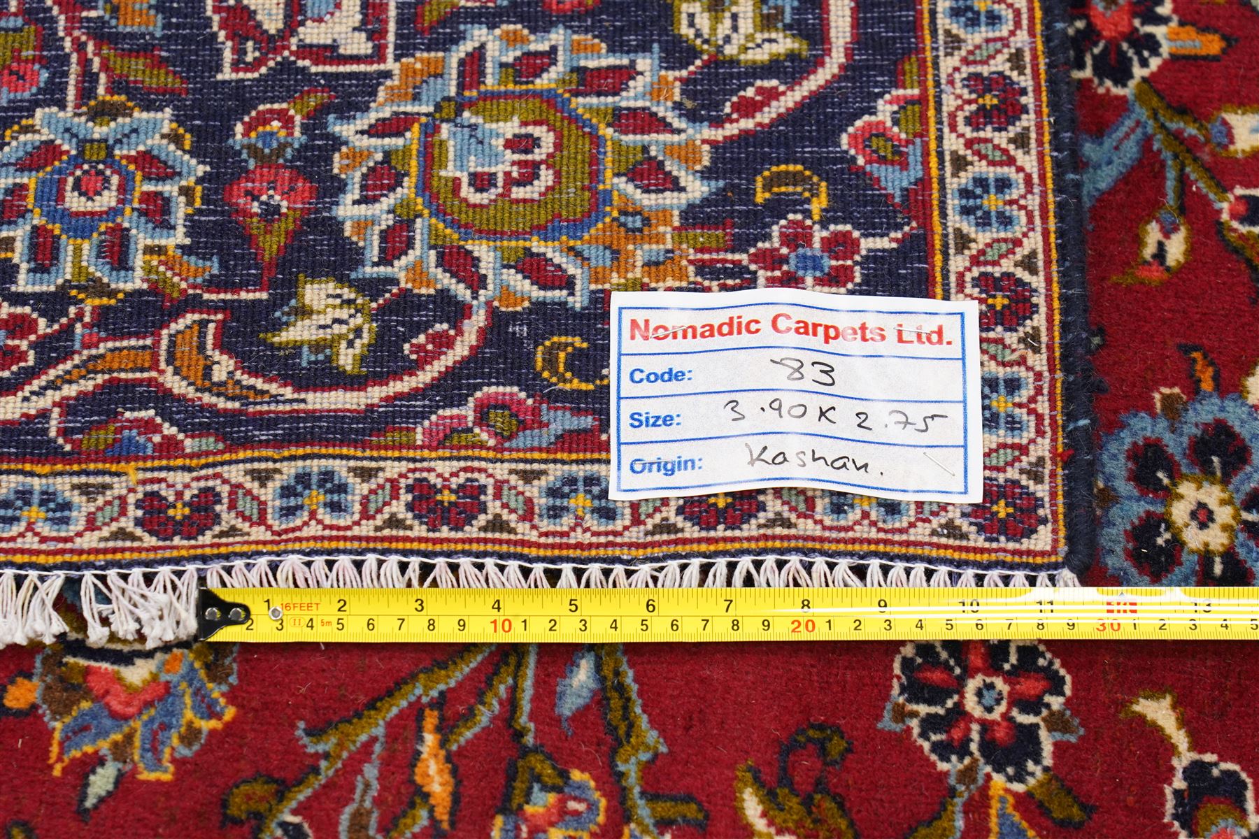 Central Persian Kashan hand-knotted carpet, crimson ground field, with central cusped lozenge medallion, enclosing a palmette and a floral rosette arrangement, surrounding field densely populated with scrolling arabesques, flowering vinery and stylized boteh motifs in tones of indigo, pale blue, ivory and ochre and spandrels of confirming design, flanked by multiple guard stripes, with cotton fringe ends 