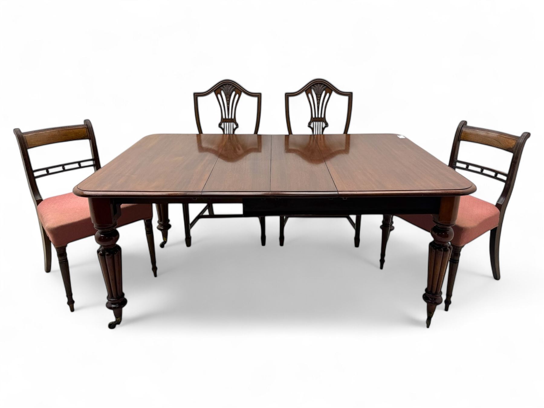 
Late Victorian mahogany extending dining table and four chairs, rectangular top with rounded corners and moulded edge, fitted with two additional leaves, raised on turned and reeded legs with brass castors, with a pair of Victorian mahogany hall chair, with curved top rail and plain splat, padded seat in textured salmon pink fabric, raised on turned and tapering front legs and another pair of early 20th century mahogany dining chair, with shield back and carved pierced splat, serpentine seat rail with striped upholstered cushion, raised on moulded square front legs