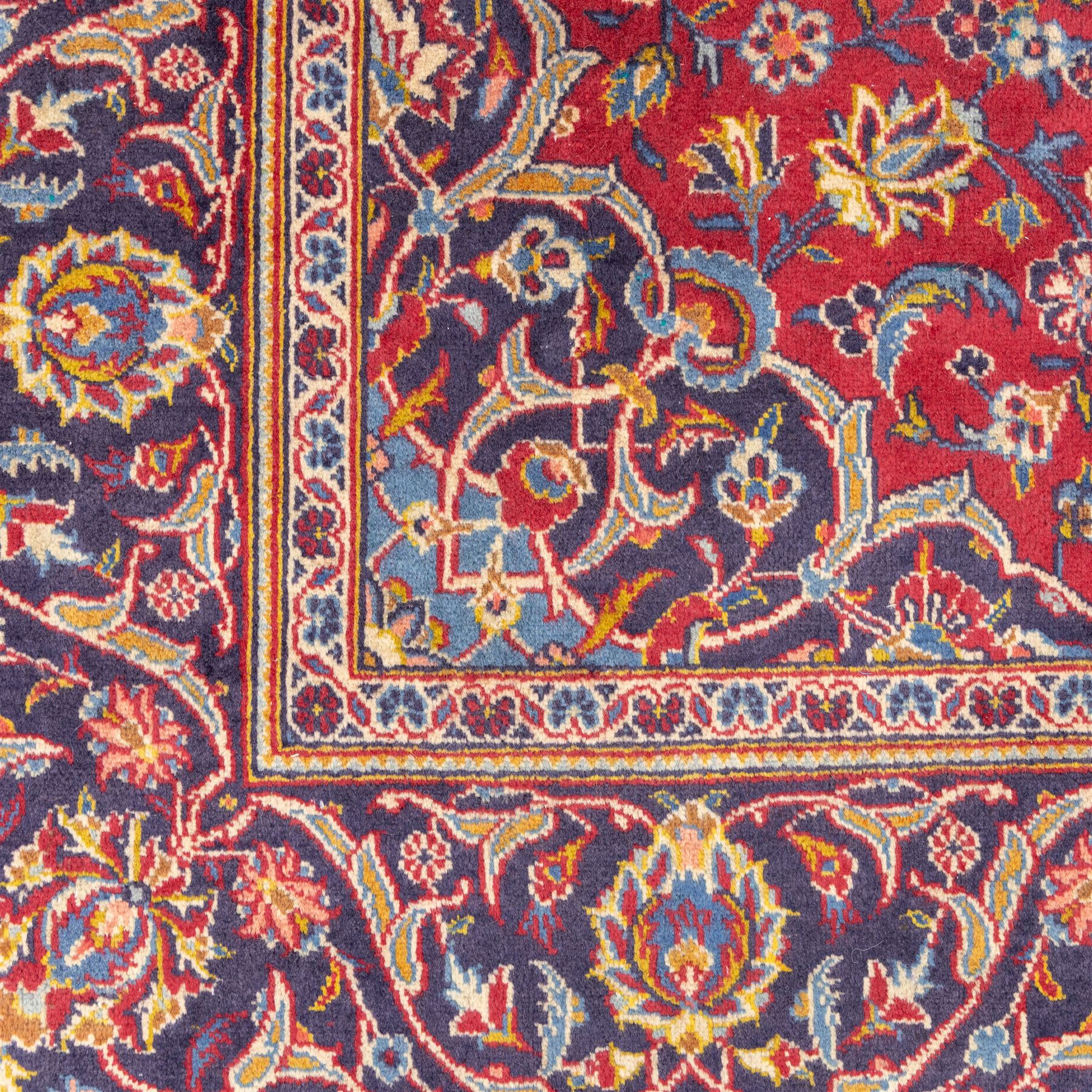 Central Persian Kashan hand-knotted rug, crimson field, profusely decorated with scrolling vines and palmettes, floral sprays around an ivory and indigo lobbed medallion enclosed by spandrels within an indigo border of arabesques between multiple guard stripes  