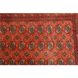 Turkmen hand-knotted carpet, madder red field, with an all-over design of row of Tekke guls, each enclosing stylized cruciform and geometric devices in tones of ivory, dark brown, and indigo, principal border of stylized geometric motifs, flanked by guard border with angular latch hook geometric designs, with cotton fringe ends 