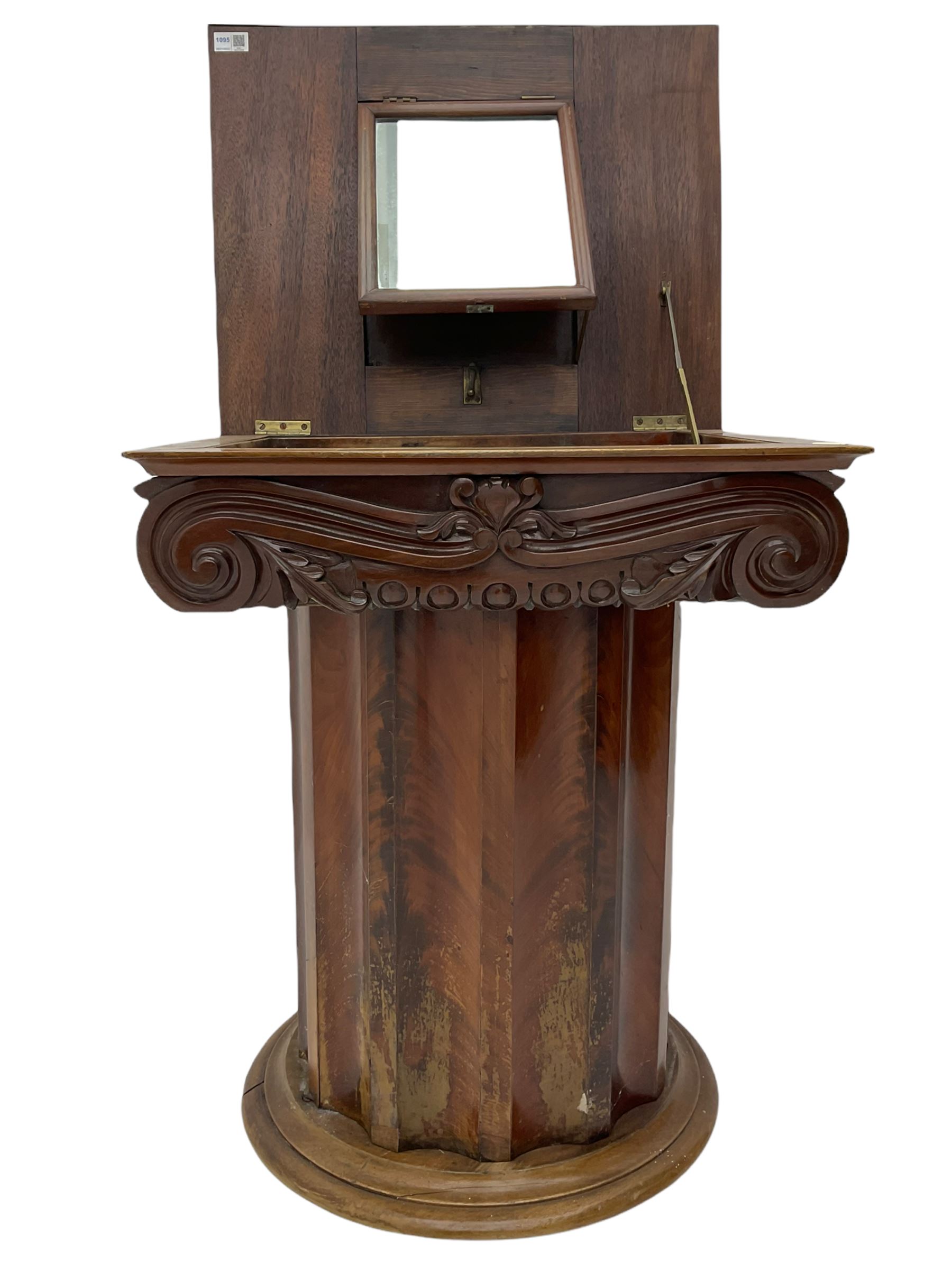 Victorian mahogany vanity unit in the form of a column, the scrolled top with hinged lid revealing mirror, wash bowl and toiletry dishes, on scalloped cylinder pedestal with single door, the interior fitted with shelf
