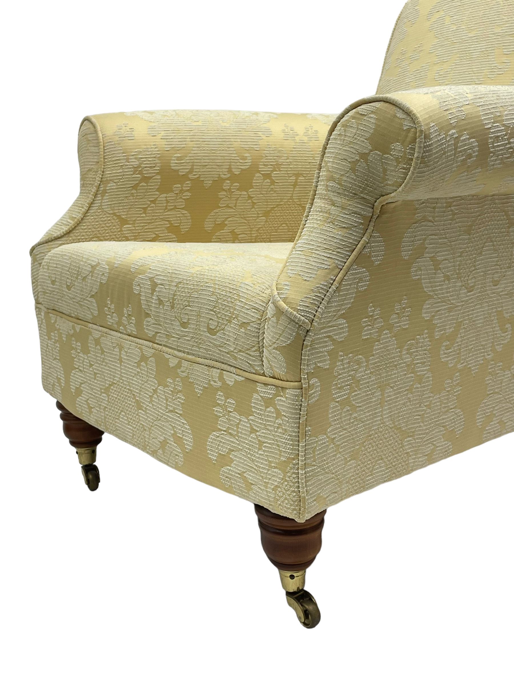 Traditionally shaped hardwood-framed armchair, rolled back and arms, upholstered in pale gold and cream damask fabric with repeating foliate pattern, on turned feet with brass cups and castors