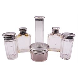 Set of six Edwardian glass dressing table jars with silver covers, comprising four facet cut cylindrical examples, tallest H13.5cm shortest H5cm, and a pair of rectangular examples, each with engraved monogram and planished effect to cover, hallmarked The Alexander Clark Manufacturing Co, Birmingham 1909