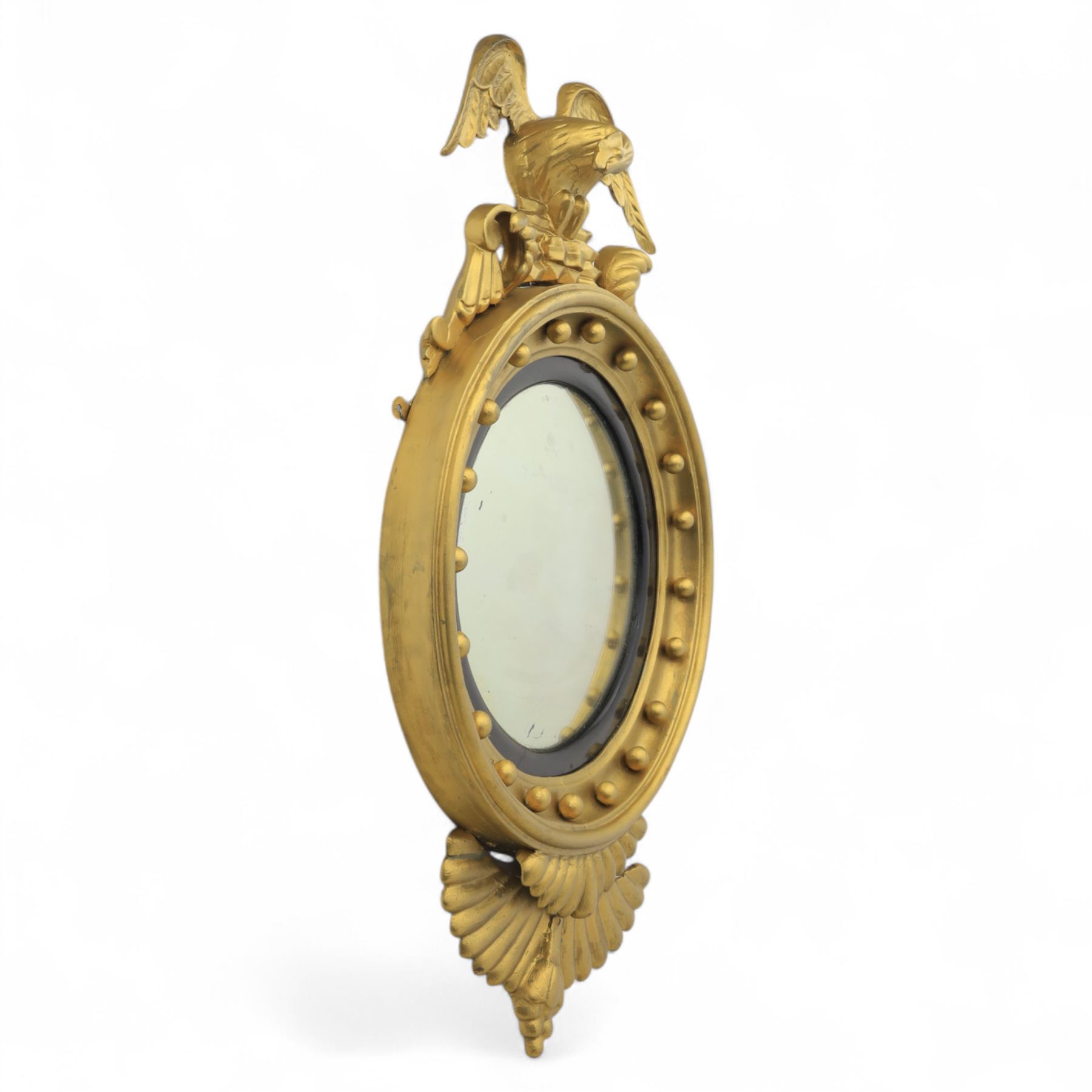 Early 20th-century Regency-style giltwood convex mirror, circular plate within a ball-mounted frame surmounted by an eagle cresting and flanked with scrolls, apron carved with foliate decoration 