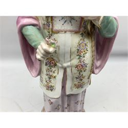 19th century continental figure of a male, modelled with a long braid and holding an opium type pipe in one hand and a flower in the other, his Chinese style dress in blue, pink and white colourway painted with deutschblumen flower sprays, raised upon blue plinth, with gilt detail throughout, with overglaze black crossed swords mark beneath, H38cm