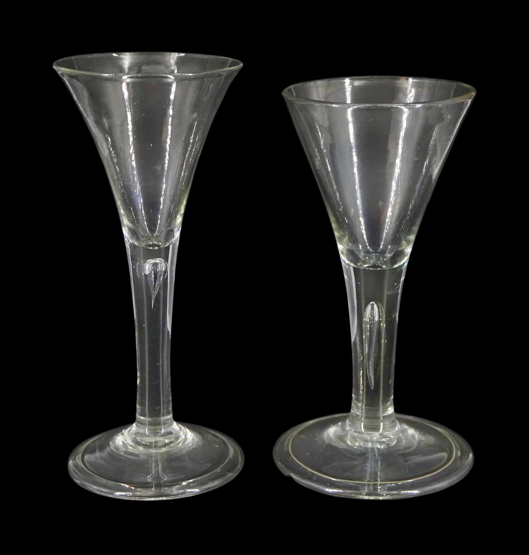 Two 18th century drinking glasses, the drawn trumpet bowls upon stems with internal tears, one elongated, and folded conical feet, largest H18cm