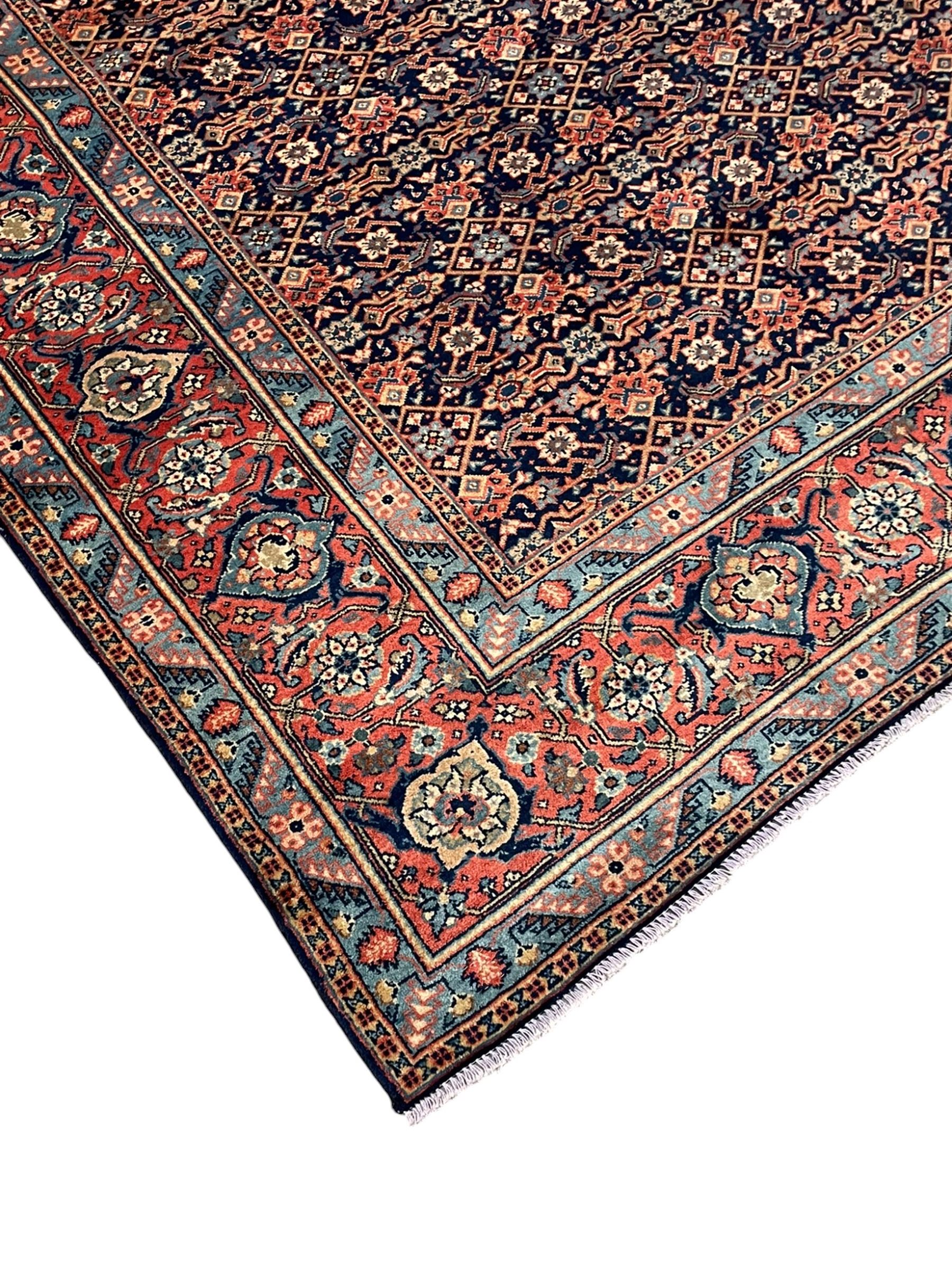 Persian Heratti indigo ground carpet, the busy field decorated with repeating floral pattern Heratti motifs, scrolling leafy branches and palmettes to the crimson ground border, within foliate pattern guard stripes 