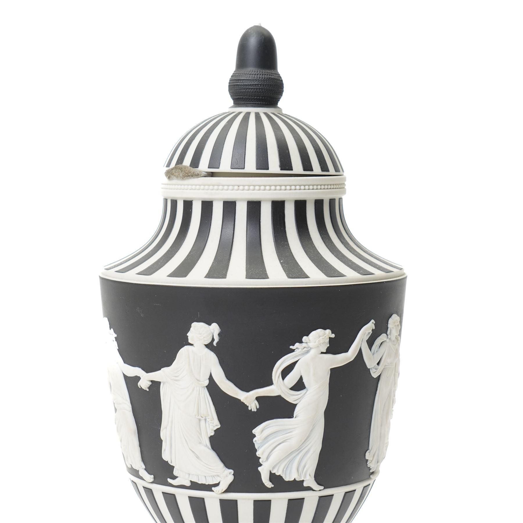 Wedgwood 20th century 'Dancing Hours' jasperware urn, the upper section decorated with a single band of neoclassical maidens in white to a black basalt ground, rising from a circular plinth decorated with foliate motifs, complete with cover with acorn finial, stamped 'Wedgwood Made in England', H25cm 
