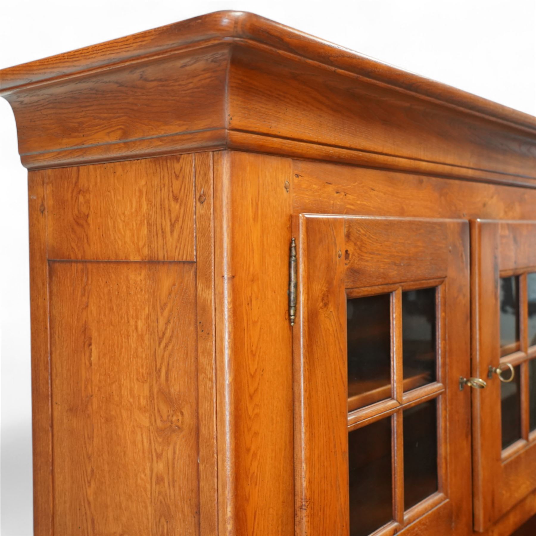Traditional design solid oak dresser, moulded cornice over twin glazed doors enclosing shelved interior, open centre section, lower base with fielded panel doors opening to shelved cupboards, on plinth base