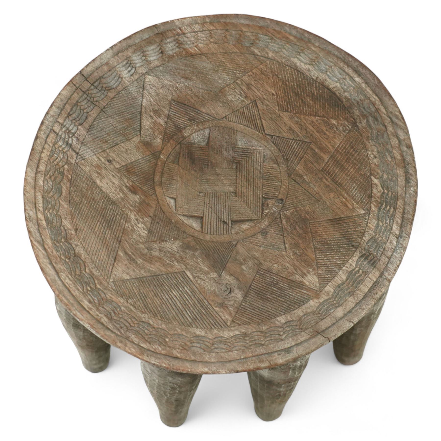 African Nupe carved tribal stool, the rounded top with repeating incised decoration and rope-edge border, supported by ten tapered legs D37cm