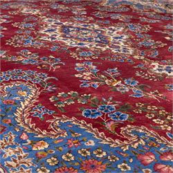 Large Central Persian Kirman hand-knotted carpet, raspberry red field, with central shaped medallion surrounded by an intricate arrangement of scrolling vines and floral sprays, within conforming spandrels and a pale blue border decorated with floral motifs, enclosed by guard stripes, with cotton fringe ends 