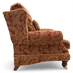 Duresta – pair of armchairs, upholstered in red and gold damask fabric with piped edges, scroll arms and loose feather-filled cushions, raised on turned wooden feet with brass castors