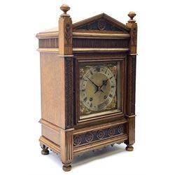  A late 19th century German eight-day mantle clock in an oak case striking the quarters and hours on two coiled gongs, going barrel movement with recoil anchor escapement, the architectural pediment with recessed tympanum and reeded frieze below, flanked by two carved full length square pillars with raised finials, square brass dial with silvered chapter ring, roman numerals and minute track, gothic steel hands and cherub face spandrels, rear case door with a sound fret representing a lyre, movement by Winterhalder and Hofmeier. 
With pendulum and Key.