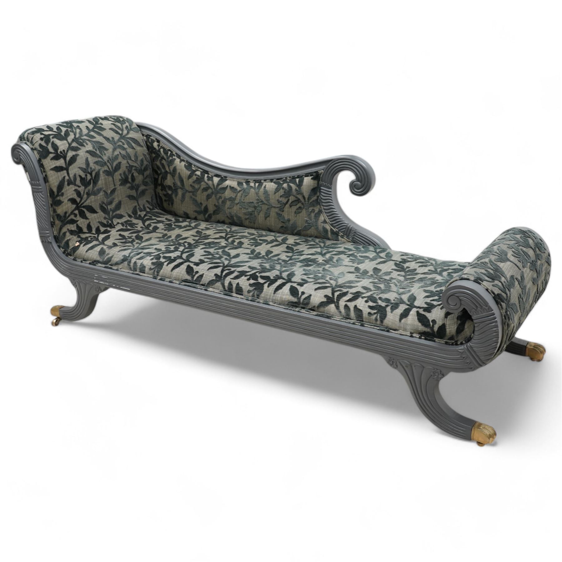 Regency design hardwood-framed chaise longue, scrolled back upholstered in leafy branch pattern fabric, reeded and scroll carved frame, on out splayed feet with brass paw castors