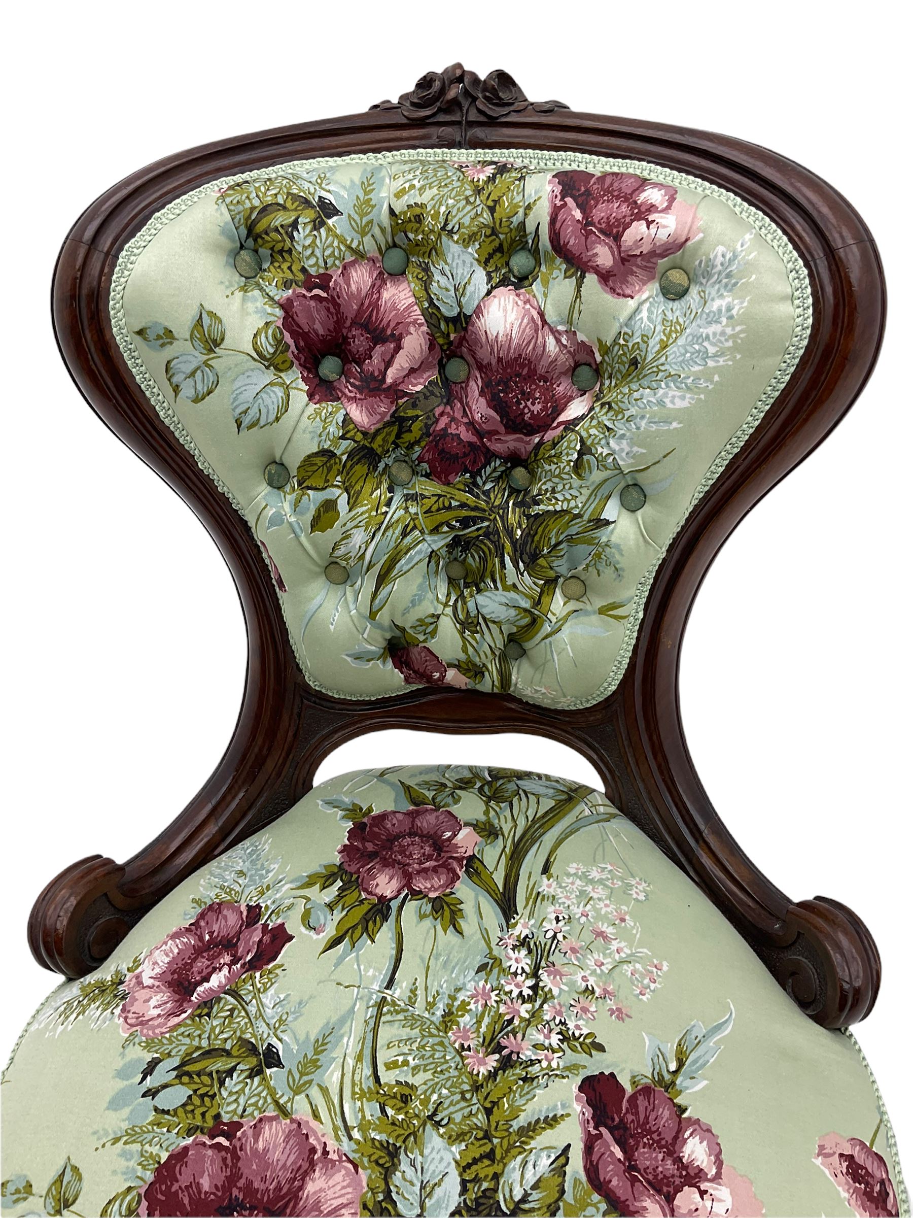 Victorian walnut framed nursing chair, spade shaped back carved with flower heads, upholstered in buttoned rose patterned fabric, on scroll carved cabriole supports terminating at brass and ceramic castors