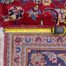 Central Persian Kashan hand-knotted rug, crimson field, decorated with an all-over floral and foliate design incorporating stylized palmettes, rosettes, and scrolling vine work, enclosed by a dark navy blue main border ornamented with flowering branches and palmettes flanked by multiple narrow guard borders with repeating floral motifs, with cotton fringe ends 