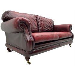Thomas Lloyd - three-piece lounge suite, comprising of traditional shape two seat sofa (W190cm H80cm) and a pair of wingback armchairs (W100cm H91cm), each with rolled arms over turned supports with brass castors, upholstered in oxblood red leather