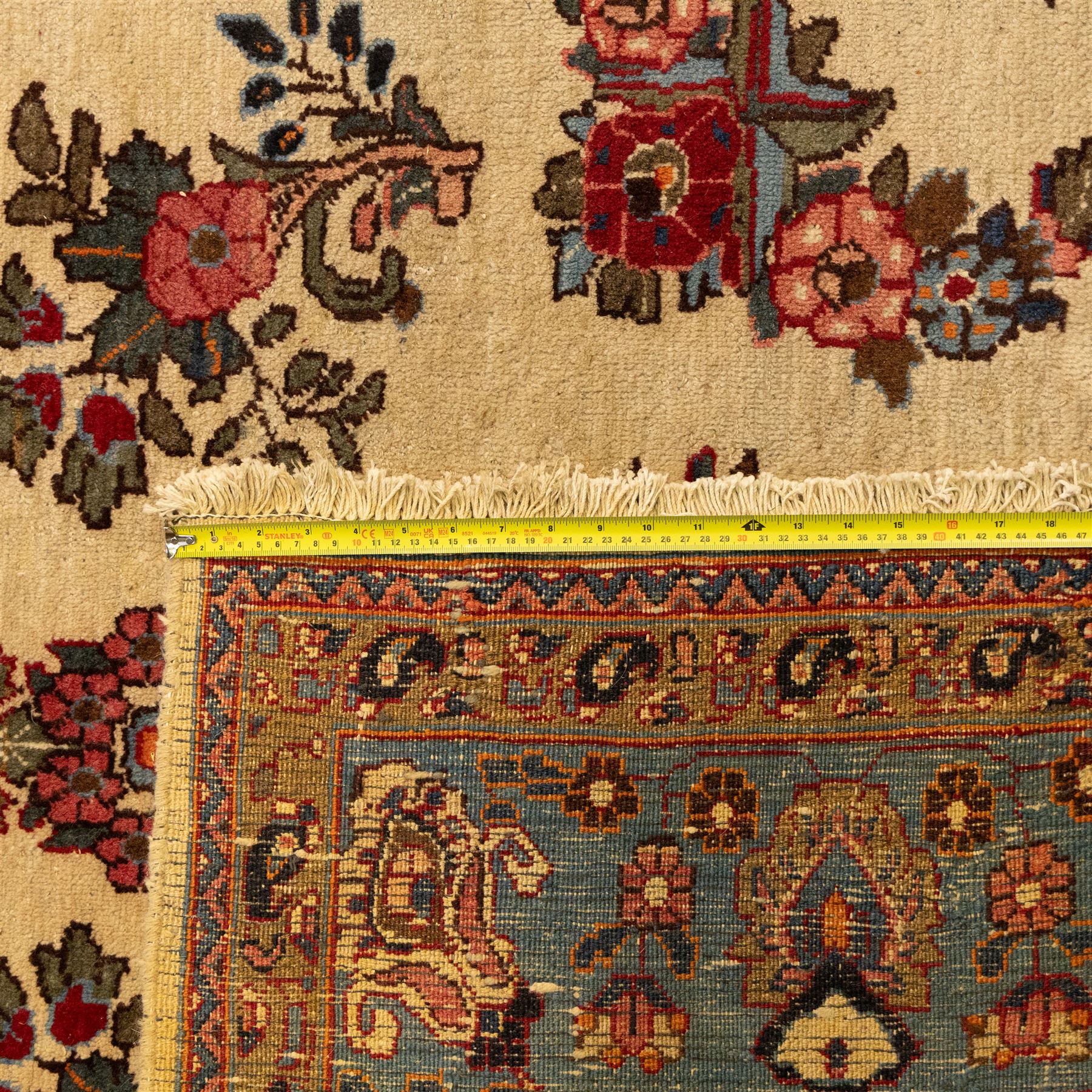Central Persian Kashan hand-knotted carpet, cream ground, with a central lobbed floral burgundy, rose, and indigo medallion, surrounded by scrolling sprays of carnations and palmettes, with sky blue spandrels decorated with curvilinear vines and stylized blossoms, framed by a repeating terracotta border of palmettes, framed by narrow guard stripes 