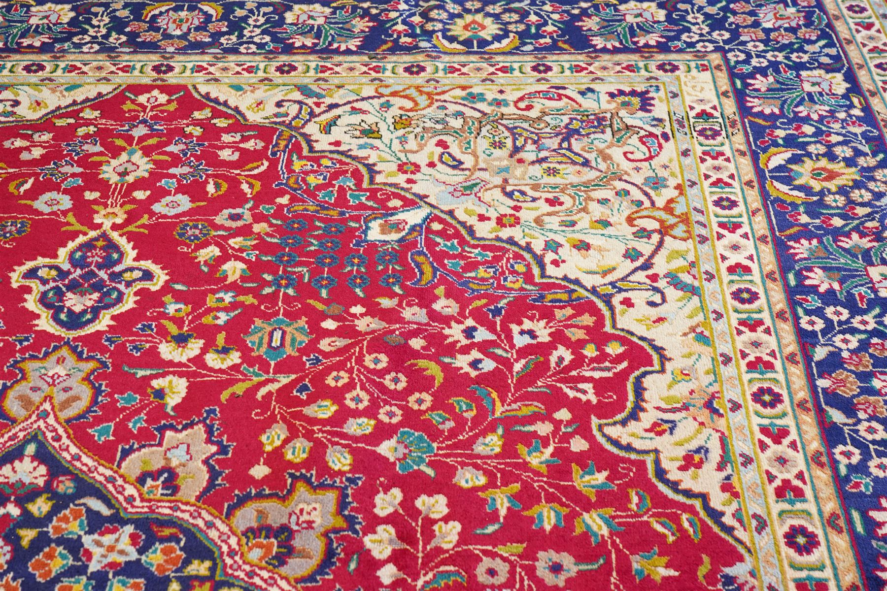 North West Persian Tabriz hand-knotted carpet, madder red field with a central cusped medallion issuing radiating pendants and an all-over design of scrolling arabesques, palmettes and flowering vinery enclosed by conforming spandrels, indigo main border of meandering floral vines and stylized palmettes, flanked by narrow guard stripes, cotton fringe ends 