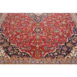 Central Persian Kashan hand-knotted carpet, crimson ground field, with central cusped lozenge medallion, enclosing a palmette and a floral rosette arrangement, surrounding field densely populated with scrolling arabesques, flowering vinery and stylized boteh motifs in tones of indigo, pale blue, ivory and ochre and spandrels of confirming design, flanked by multiple guard stripes, with cotton fringe ends 