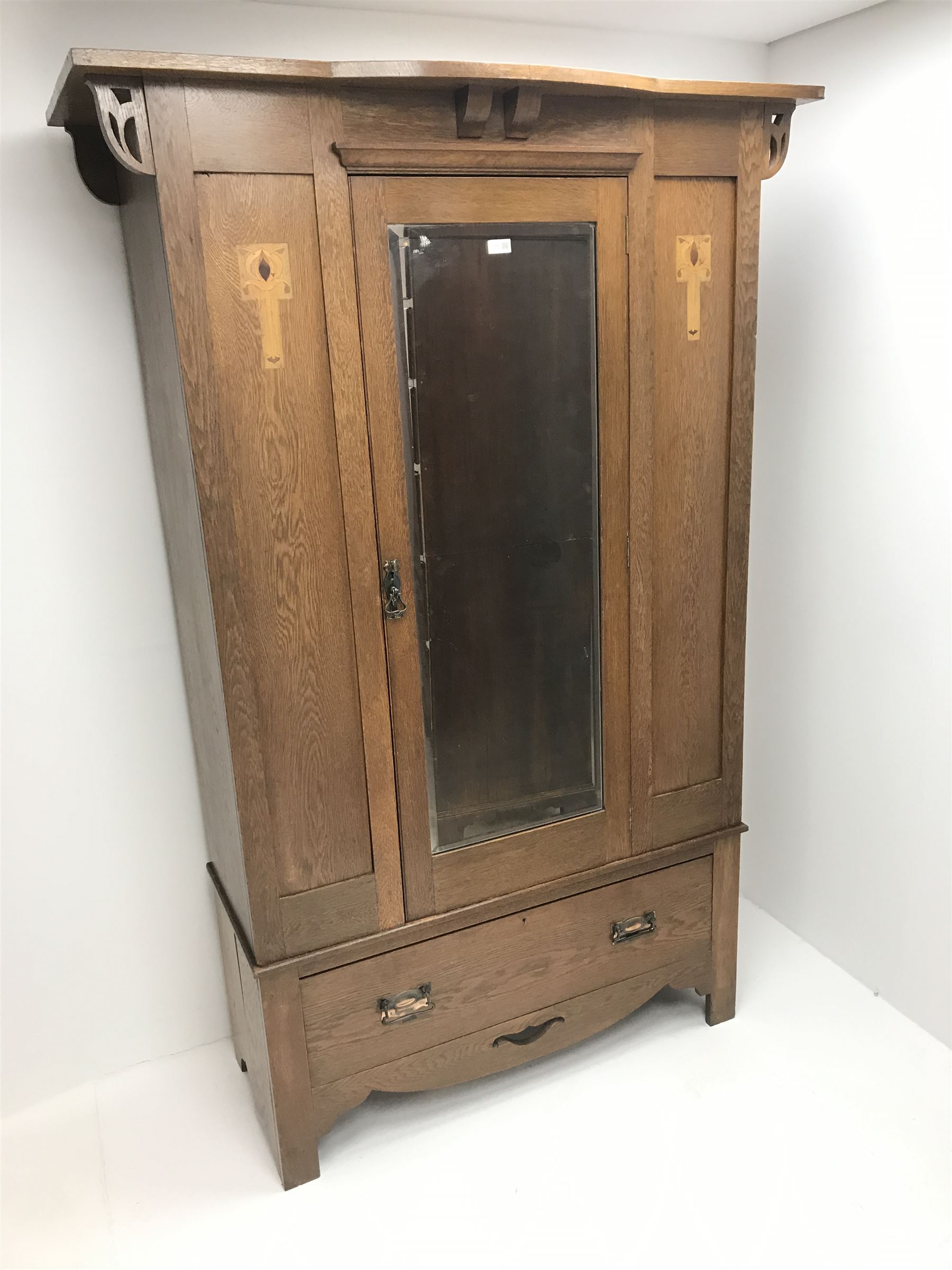 Arts and Crafts period oak wardrobe, projecting shaped cornice, single bevel edged mirrored door above drawer