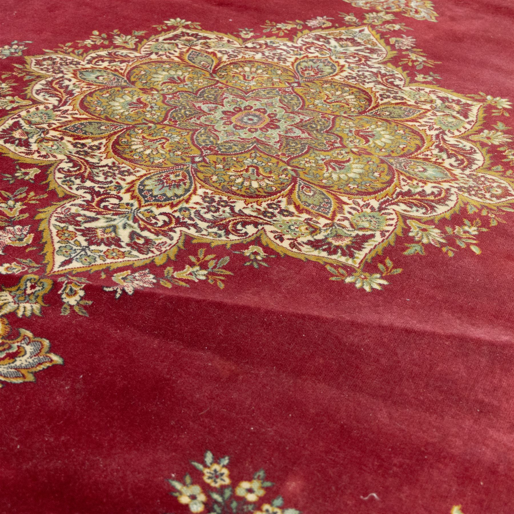 Kashan design carpet, crimson field with central medallion and scrolling floral sprays, cream and polychrome palmette and scrolling vine borders  