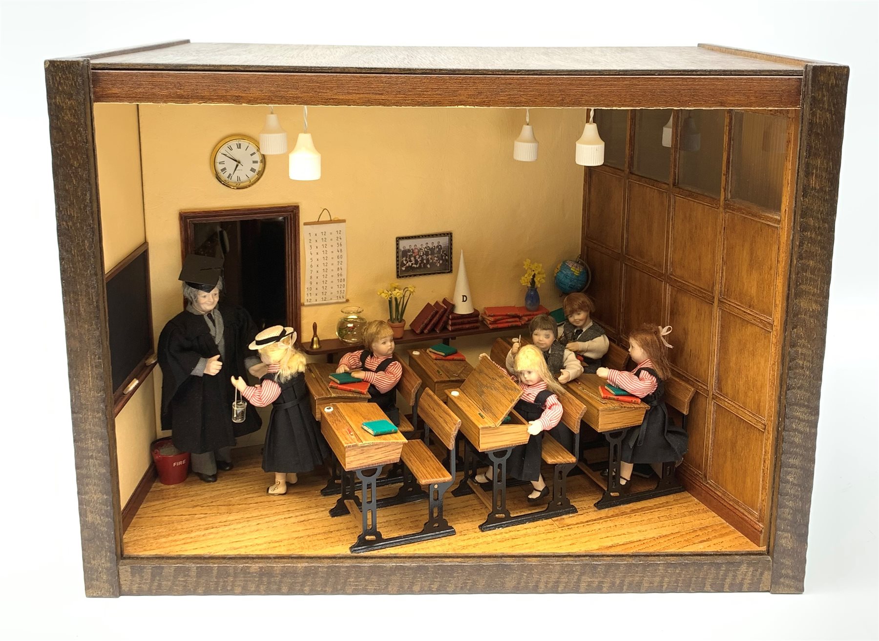 A 1/12th scale diorama of a school room interior, depicting pupils and teacher, the room furnished with panelled wall, desks, chalk board, globe, books and dunces hat, etc., H29cm L40cm D26cm.  
 
This model is based on a Victorian School Room in the museum in Armley, where the children and teachers would dress in period costume and attend lessons during the summer time.