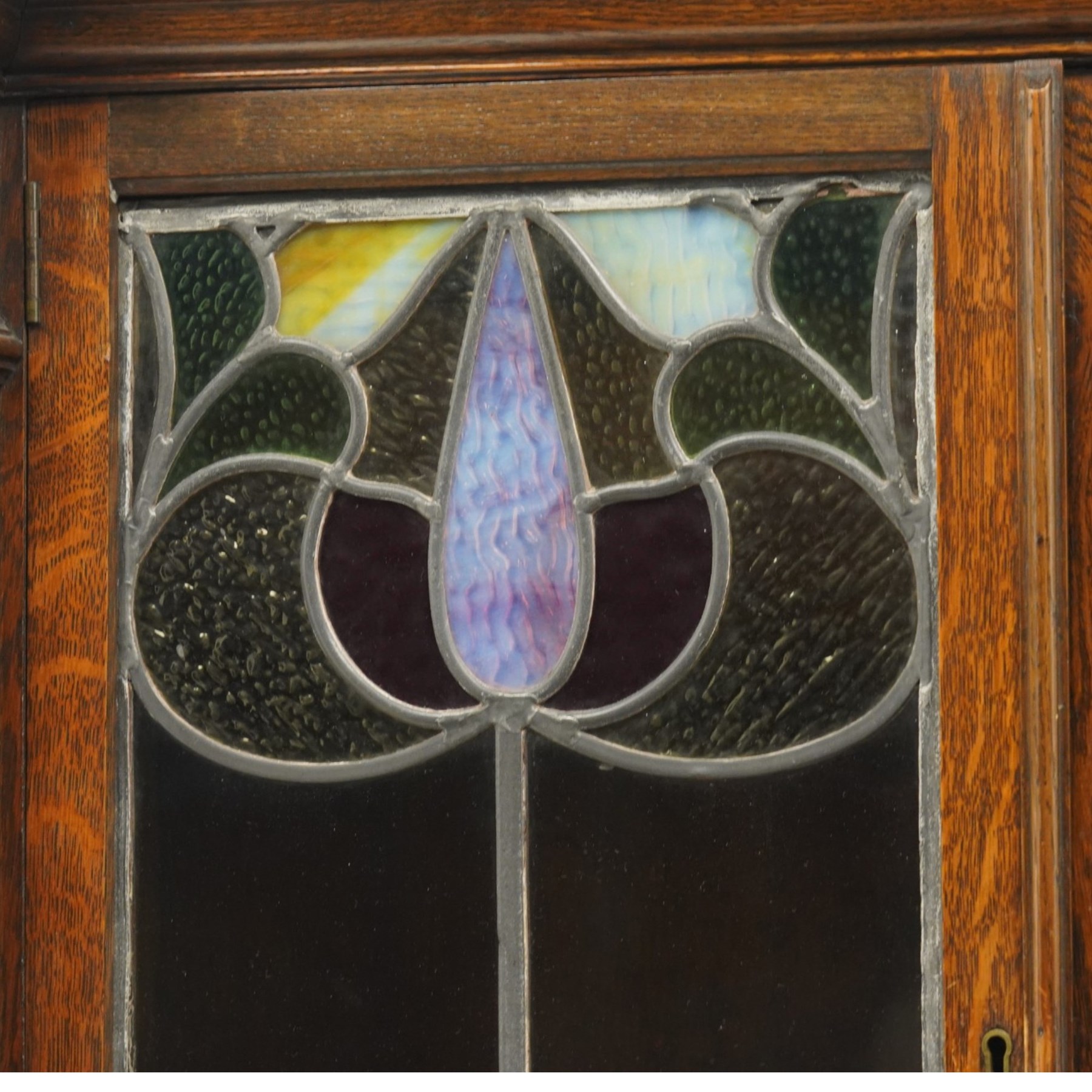 Arts and Crafts oak dresser, projecting moulded cornice above three glazed panels with coloured leaded glass floral panels, flanked by two glazed doors enclosing two adjustable shelves, open mirrored recess below with mirrored back, the base fitted with two short drawers over two central drawers flanked by carved panelled cupboard doors, ornate brass handles, raised on tapering square legs