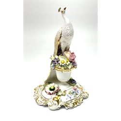 A Royal Crown Derby porcelain figure, modelled as a peacock perched upon an urn of encrusted flowers, upon a scrolling base with scrolling gilt and encrusted flower decoration, with printed mark beneath, with makers box, H24cm. 