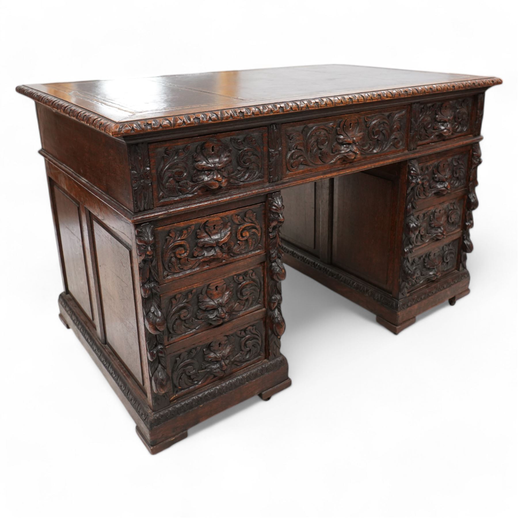 Victorian carved oak twin pedestal desk, moulded and foliate carved rectangular top with leather inset, fitted with nine drawers, each carved with scrolling foliage and lion mask handles, on skirted base 