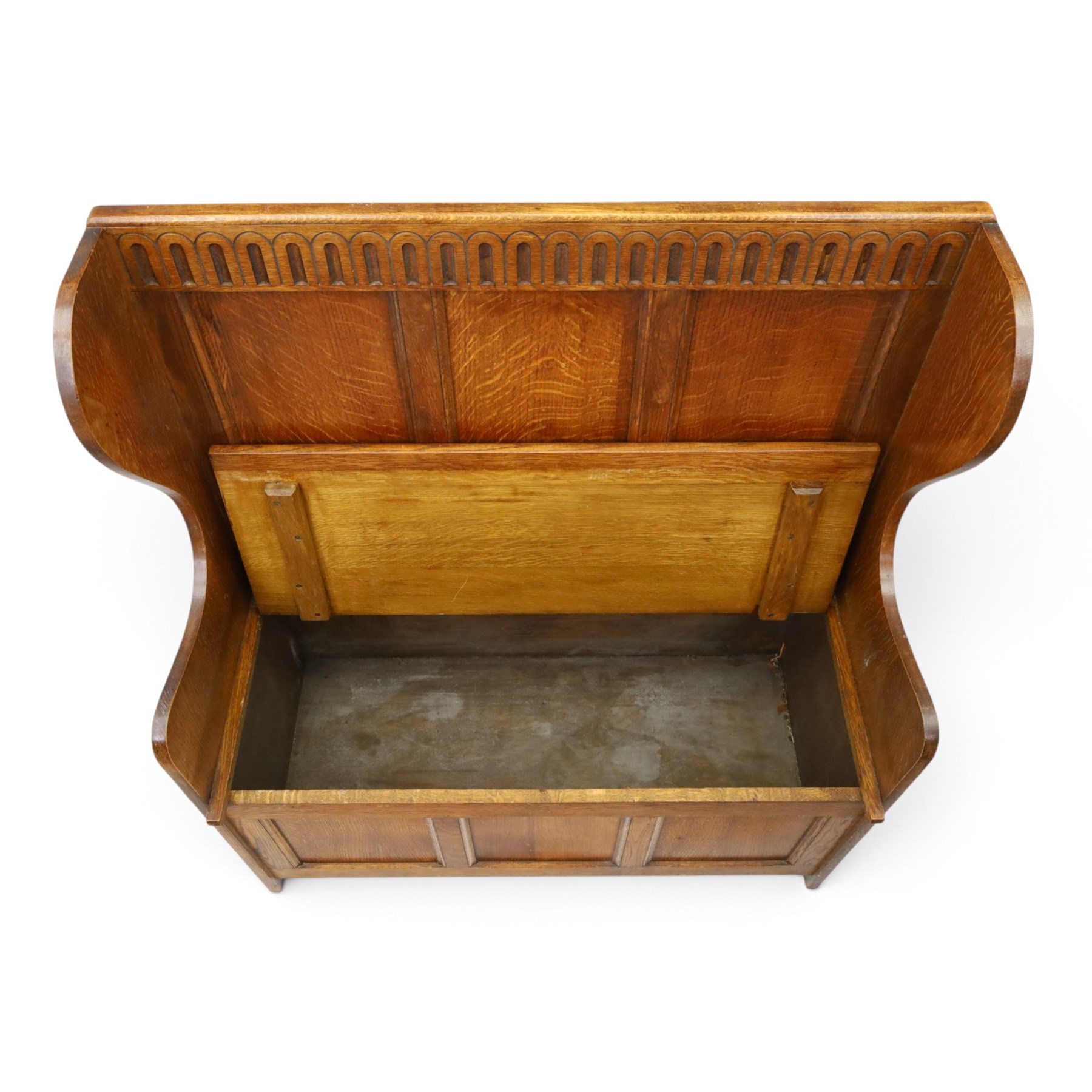 Early 20th century oak box settle, panelled back with arcaded carved rail, swept sides and arms, hinged seat with storage, panelled front