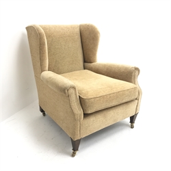  Edwardian low wingback armchair, upholstered in a beige fabric, square tapering supports brass castors, W75cm  
