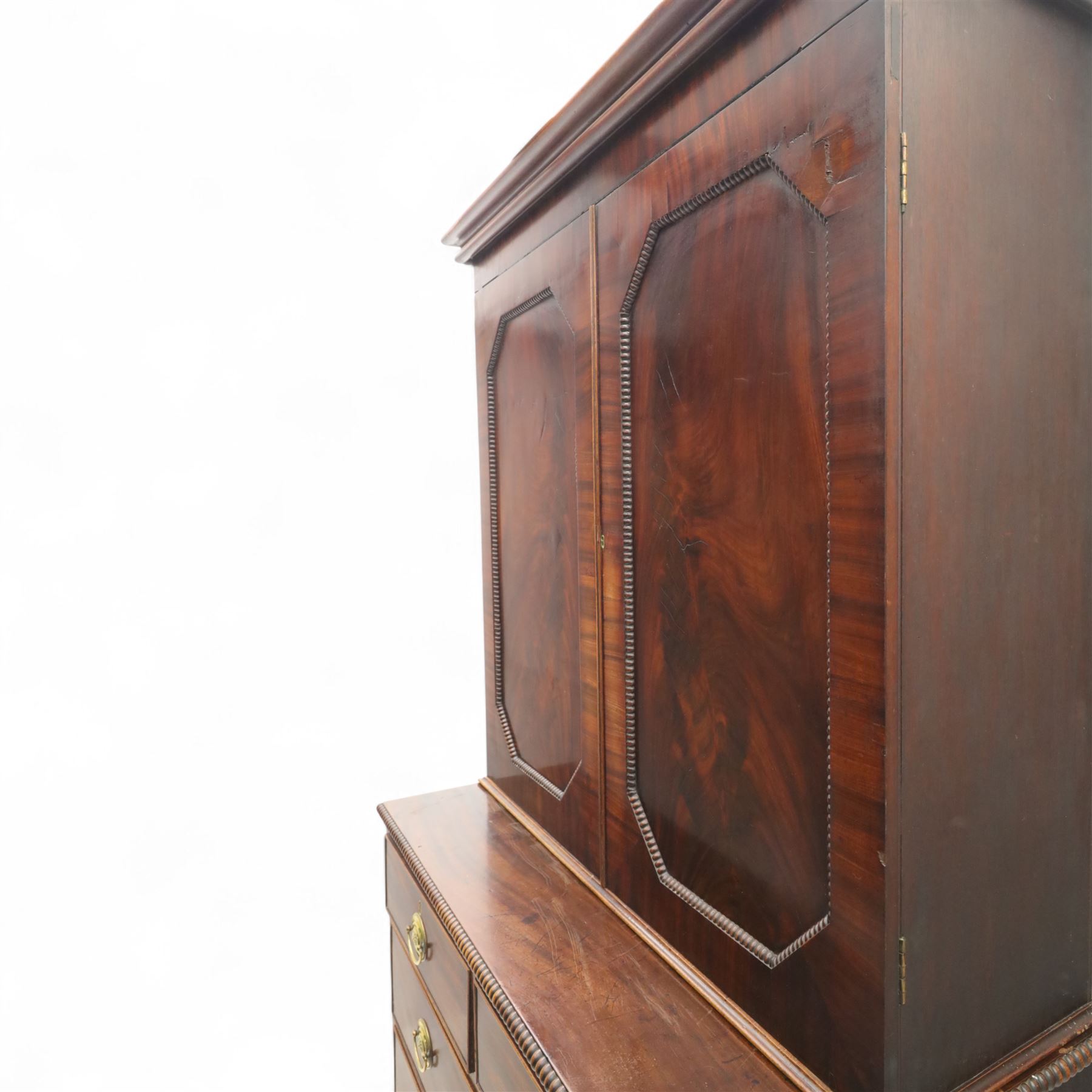 George III mahogany linen press, moulded cornice above a pair of panelled doors with gadrooned beading above a gadrooned edge over two short and three graduated drawers, with shaped apron, raised on sabre feet  