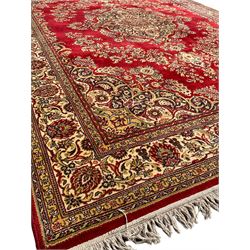 Persian design crimson ground carpet, central rosette medallion surrounded by clusters of flower head motifs, scrolling floral design spandrels, the border decorated with repeating stylised plant motifs within guard stripes 